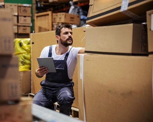 bearded-tattooed-hardworking-blue-collar-worker-overalls-crouching-storehouse-using-tablet-checking-inventory_232070-11572
